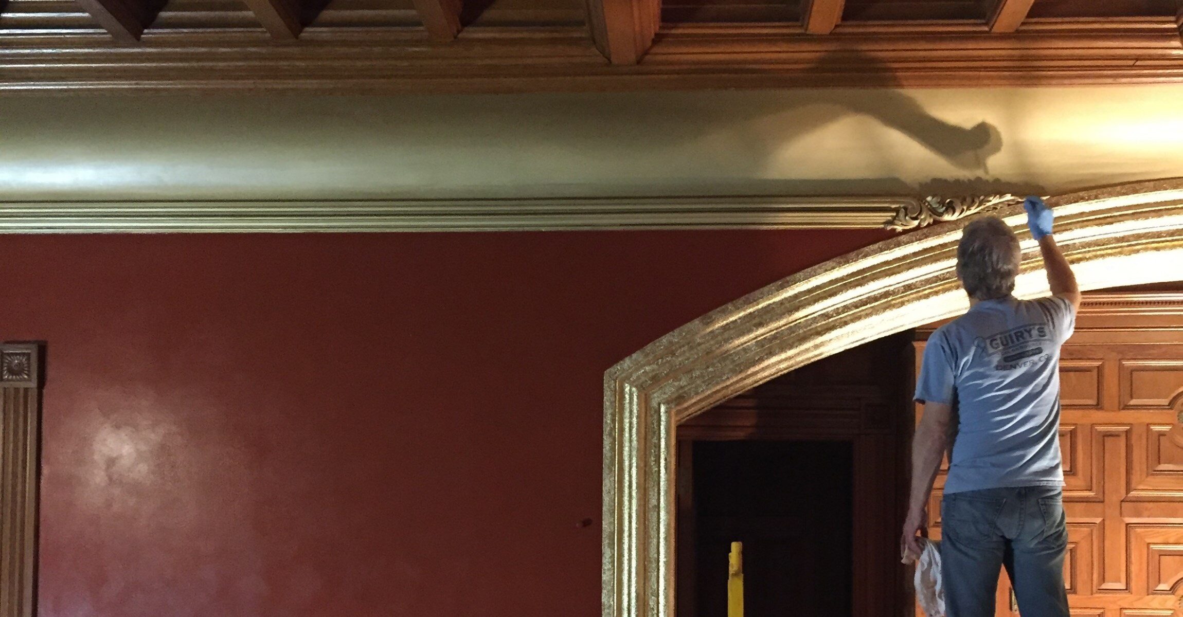 Man applying gold leaf to large archway.