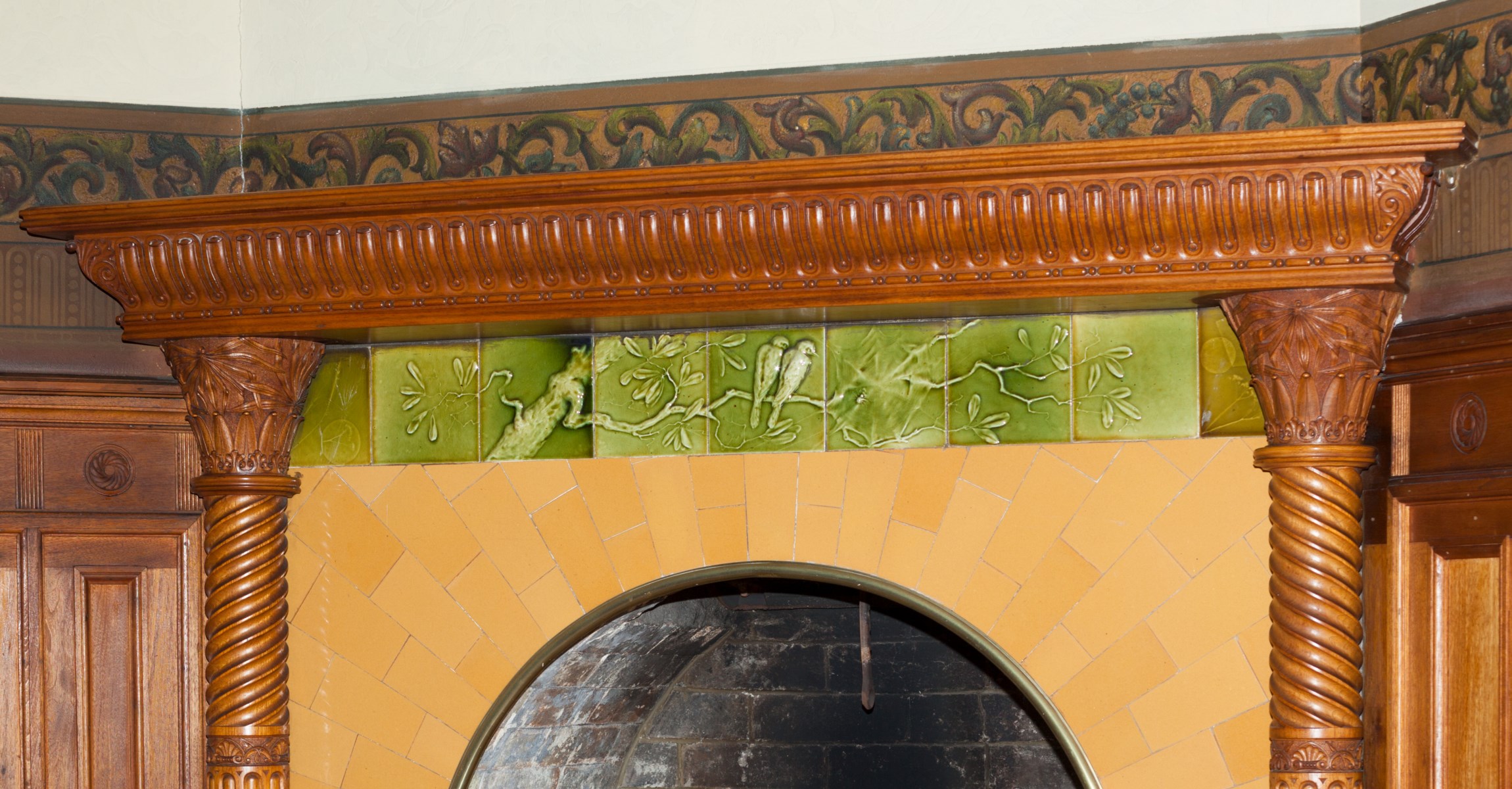 View of wooden mantle with lime green decorative tile frieze of  birds on a branch and cobweb.