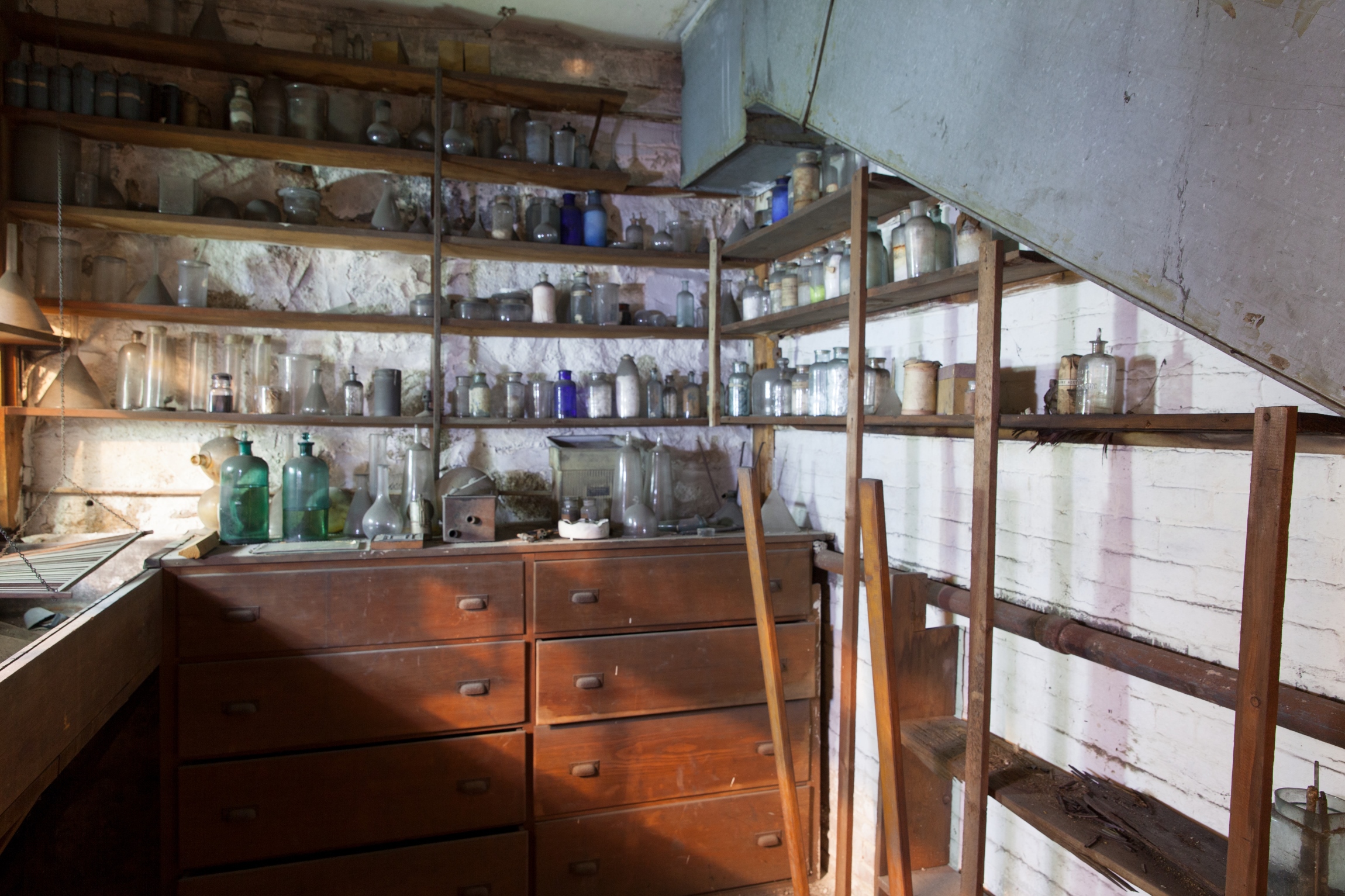 Shelves lined with bottes and vials, above wooden drawers with a metal tub along one side.