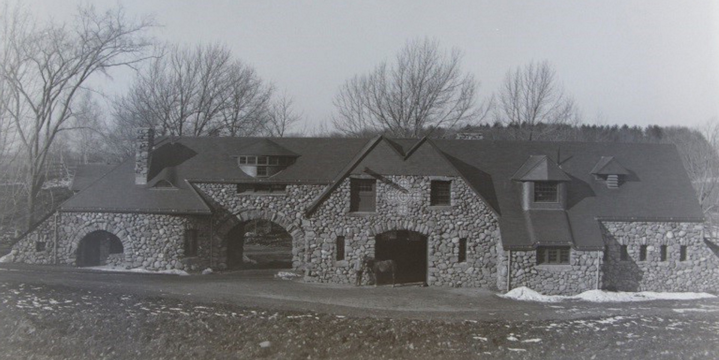 Black and white photograph of stone gatehouse building with arched entrances. Some snow on the ground.