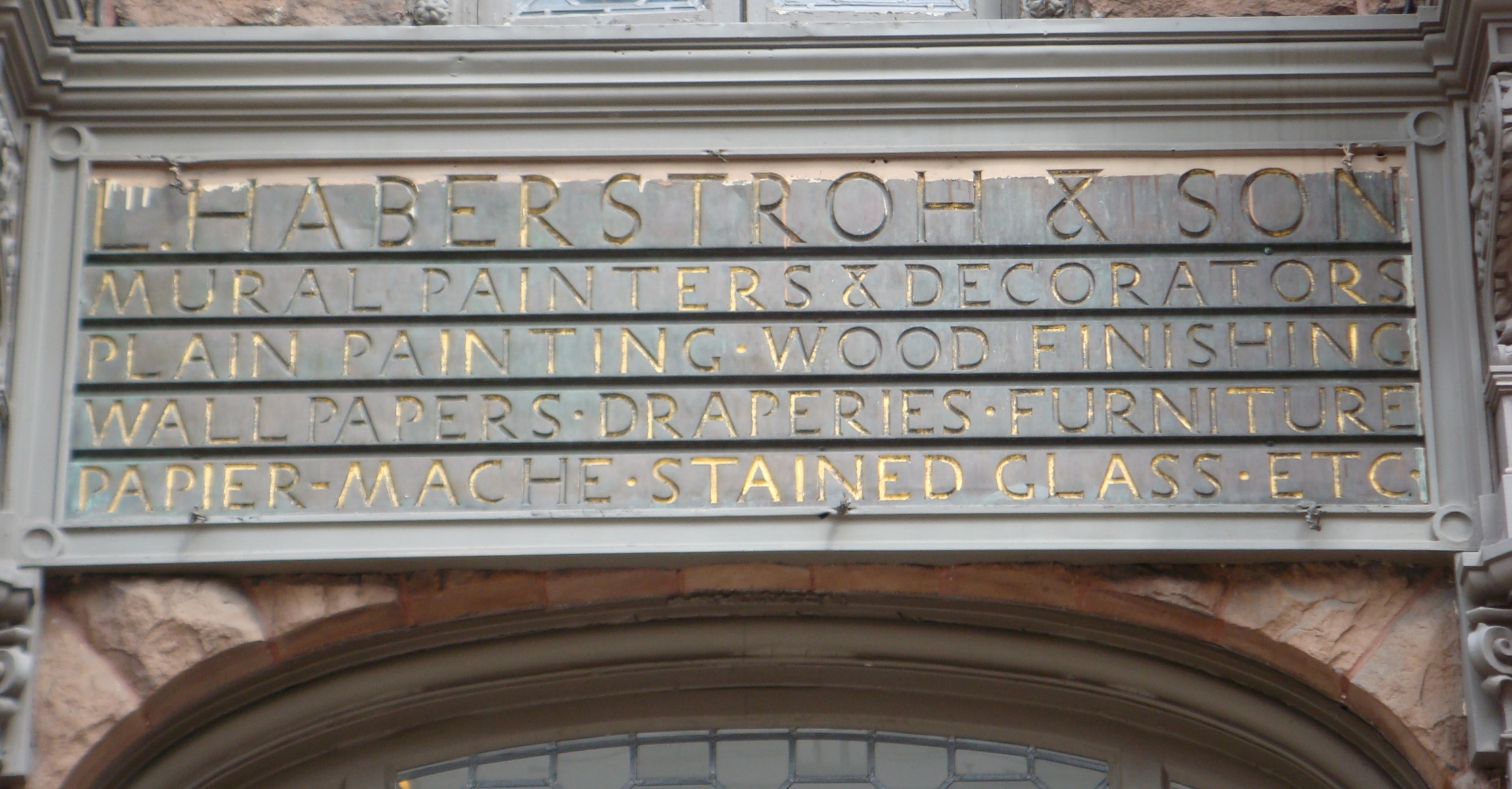 Wooden sign over arched doorway, text in gold reads: L. Haberstroh & Son, Mural painters & decorators, plain painting, wood finishing, wall papers, draperies, furniture, papier-mache, stained glass, etc.