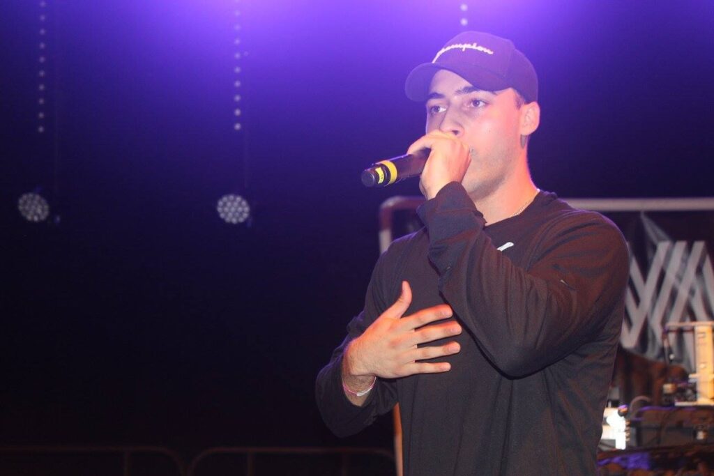 Man wearing hat speaking into a microphone.