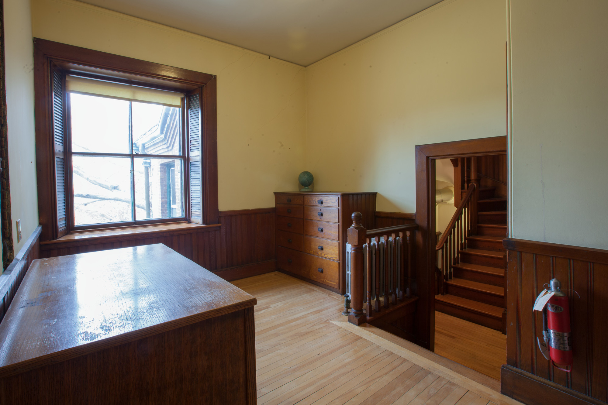 Room with a window, dresser, and open door with view of stairs beyond.